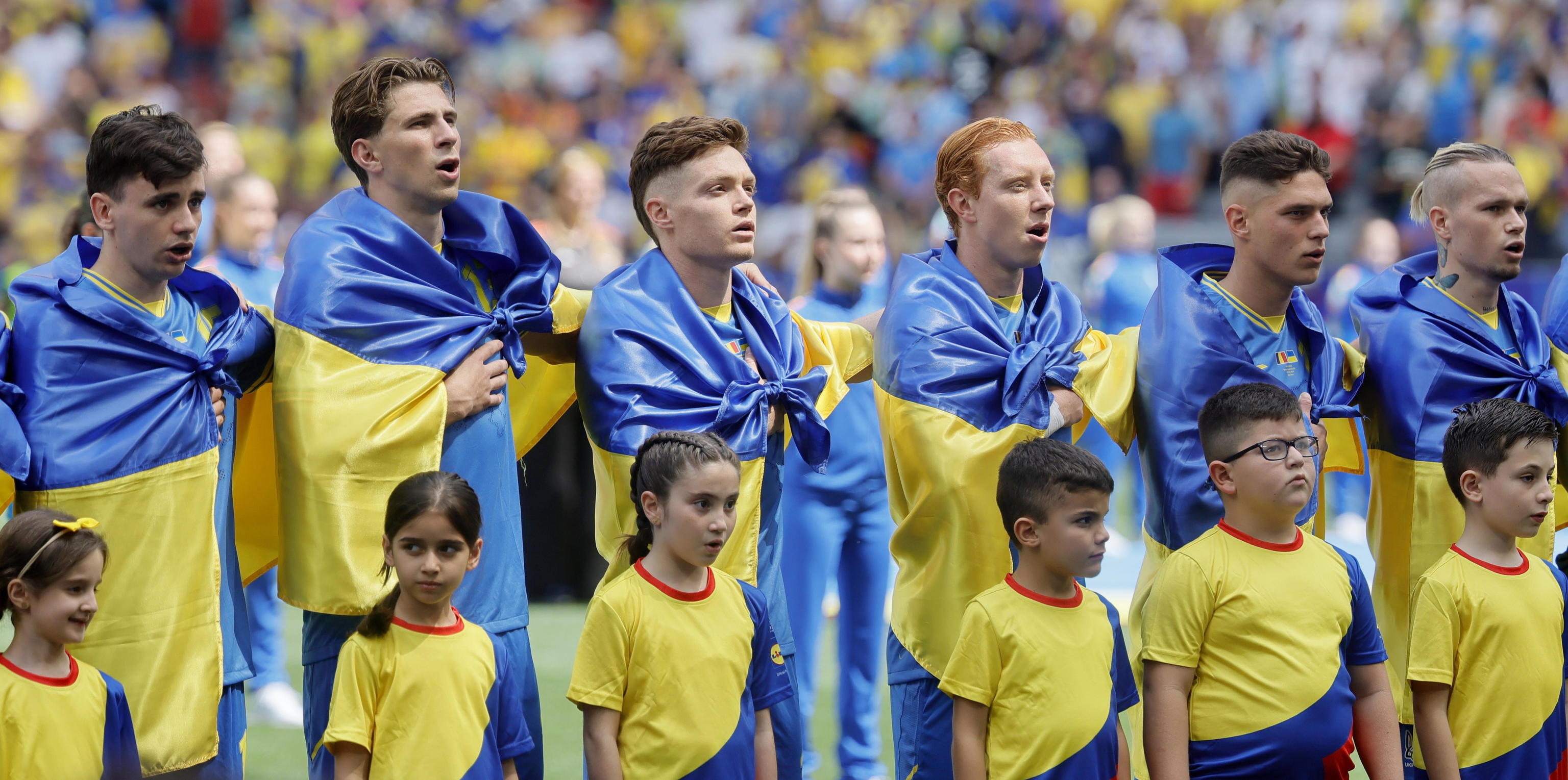 La selección de Ucrania escucha el himno con la bandera atada al cuello